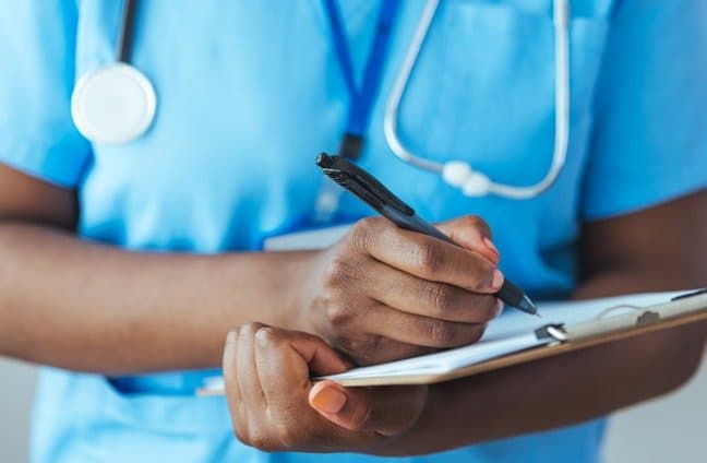 A nurse in scrubs writing notes on a clipboard