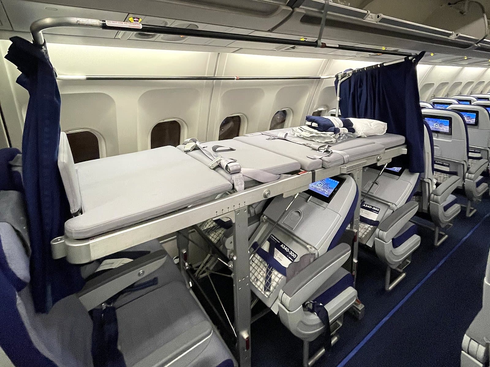 An airline stretcher installed over a row of economy seats, with privacy curtains, on a scheduled widebody flight